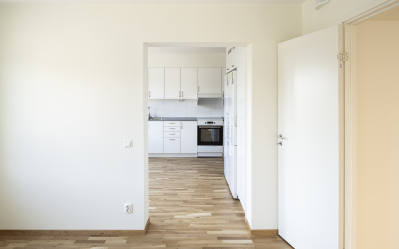 Ett tomt kök med vita skåp och trägolv.